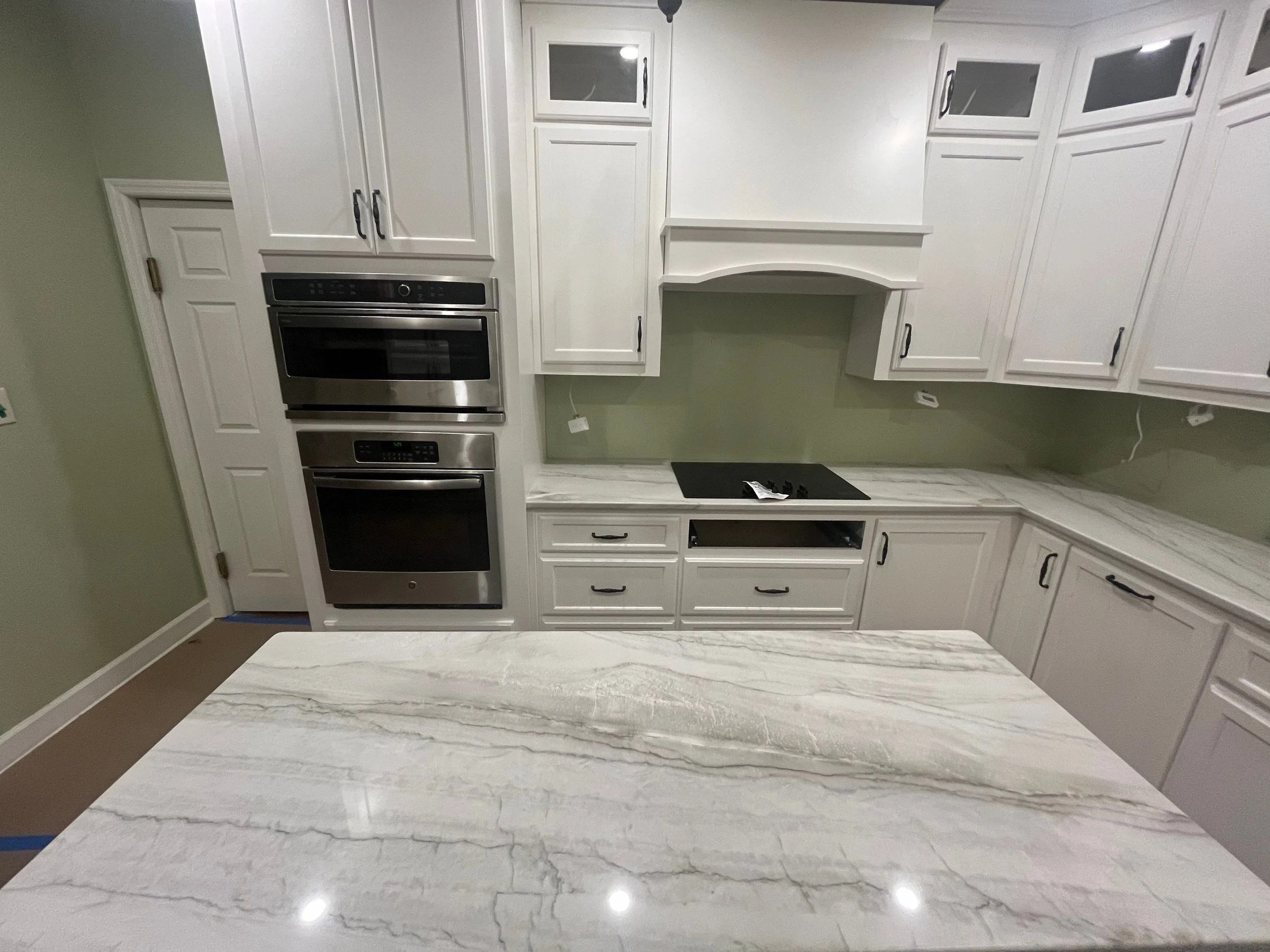 Kitchen with white cabinets, stainless steel double oven, black cooktop, and a marble countertop island.