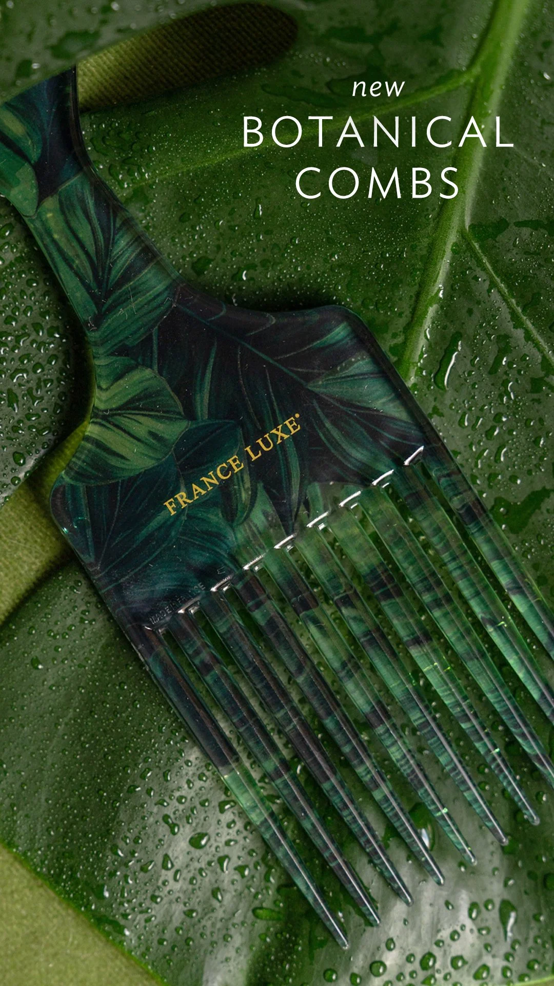 A black hair comb with green leaf patterns and the words 'France Luxe' in gold, placed on a wet green leaf background.