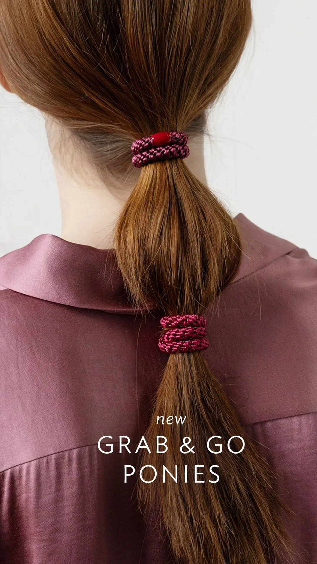Close-up of a person's brown hair tied in a low ponytail with pink and black scrunchies, wearing a mauve-colored satin shirt.
