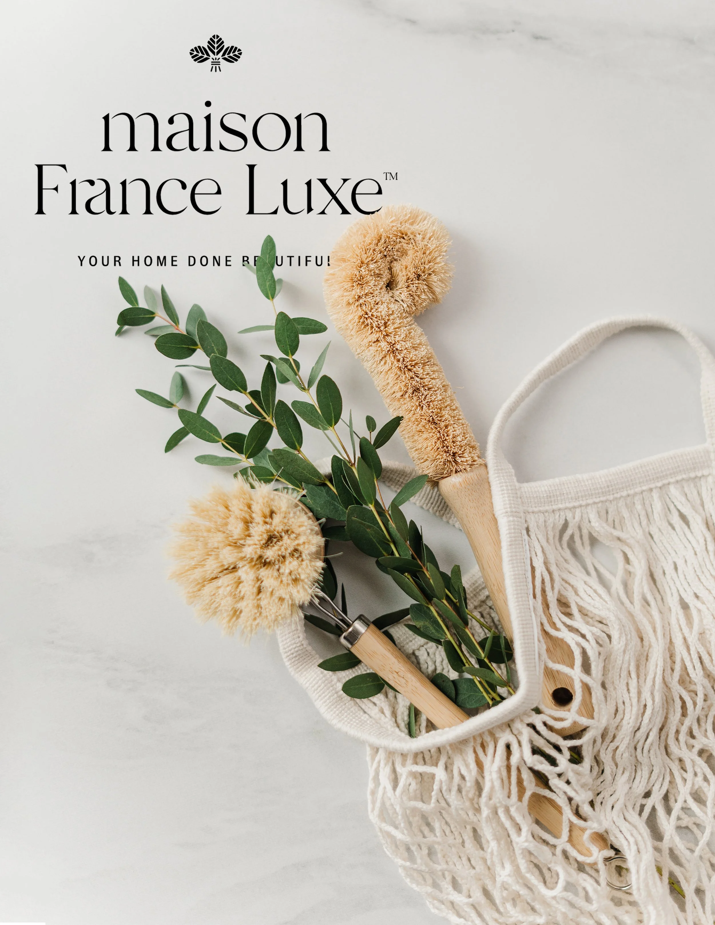 A skincare or beauty product brochure with the name "maison France Luxe" at the top, featuring the tagline "Your home done beautiful!" Beneath the text, there is a beige bath brush with natural bristles, a sprig of green leaves, and a small section o