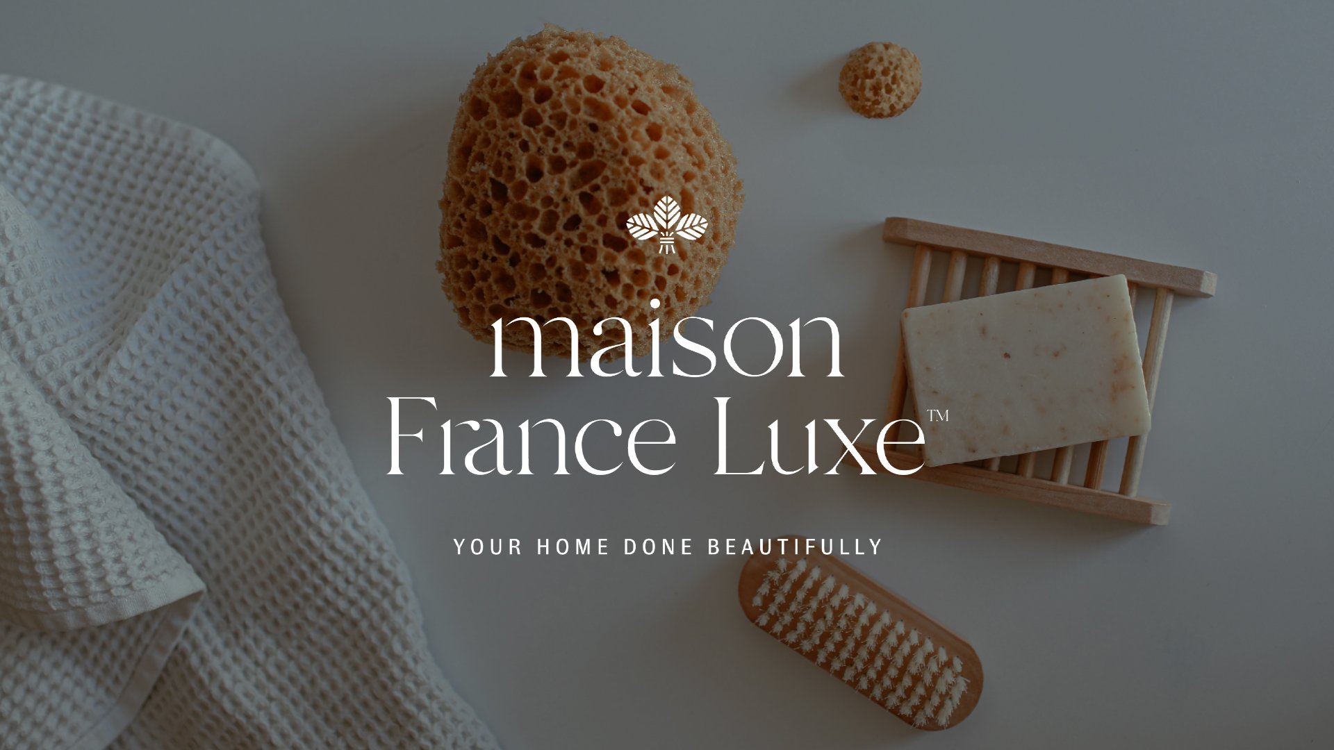 Flat lay of spa or skincare items including a hydrating sponge, bar soap on a wooden soap dish, a textured cloth, and a toothbrush, with overlay text for Maison France Luxe.