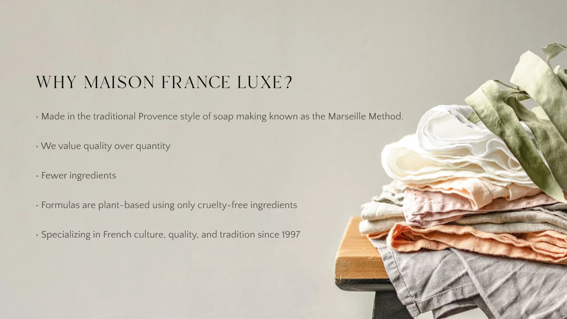 A promotional image for Maison France Luxe featuring a beige background with black text and a stack of folded, pastel-colored fabrics on a wooden stand on the right side.
