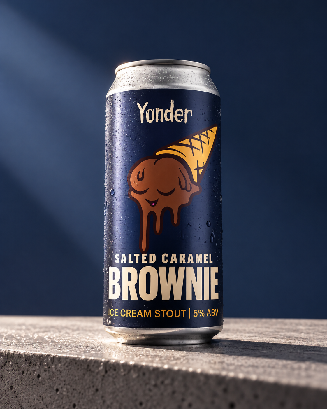 Can of Yonder Salted Caramel Brownie Ice Cream Stout beer with cartoon brownie ice cream cone on label, condensation on can, on a stone surface with a dark blue background.