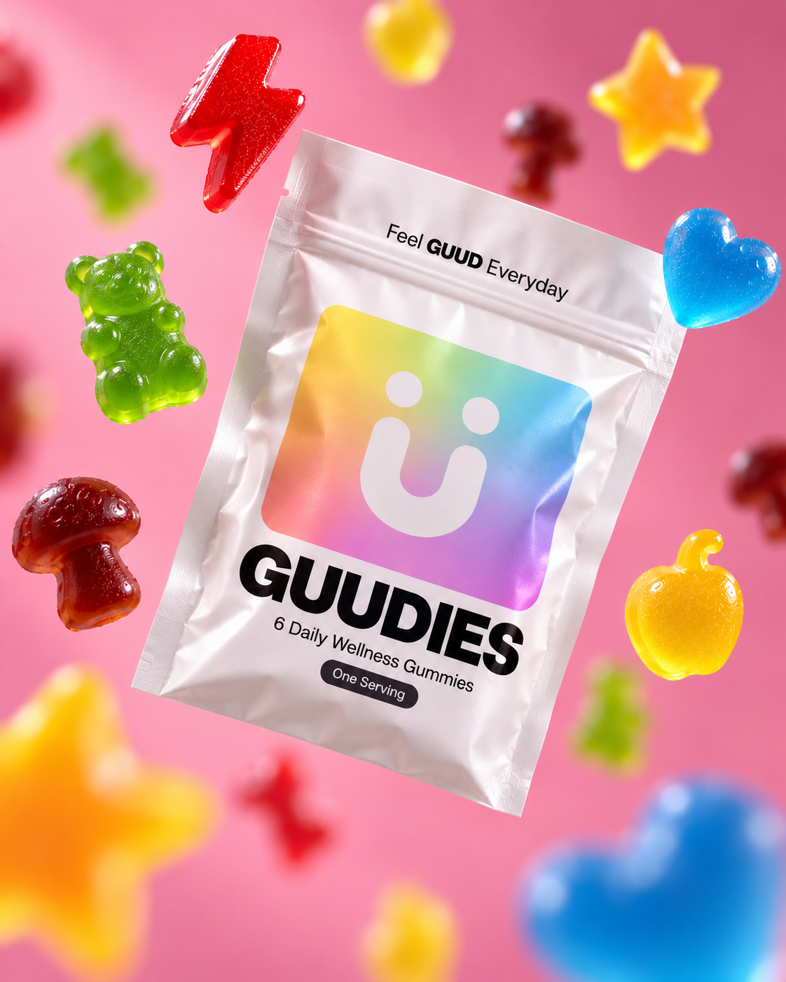 A bag of GUDIES wellness gummies surrounded by colorful gummy candies in various shapes against a pink background.