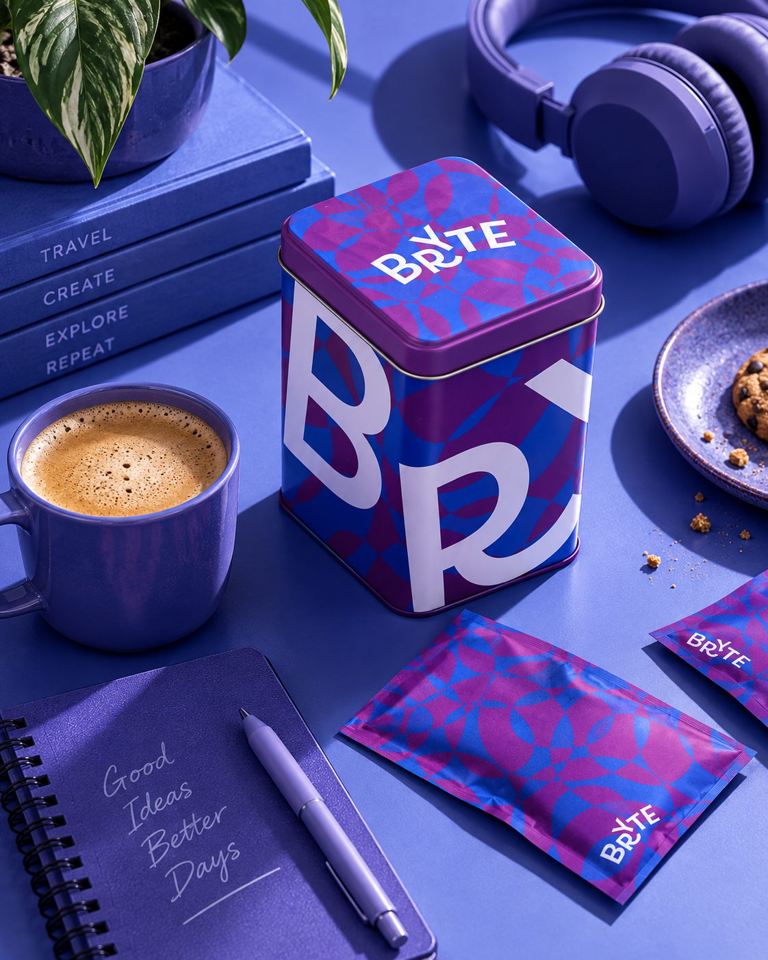 A blue workspace with a plant, a cup of coffee, a notebook with the words 'Good Ideas Better Days,' a pen, a tin labeled 'Byte,' blue headphones, a snack on a blue plate, and packets with the Byte logo.