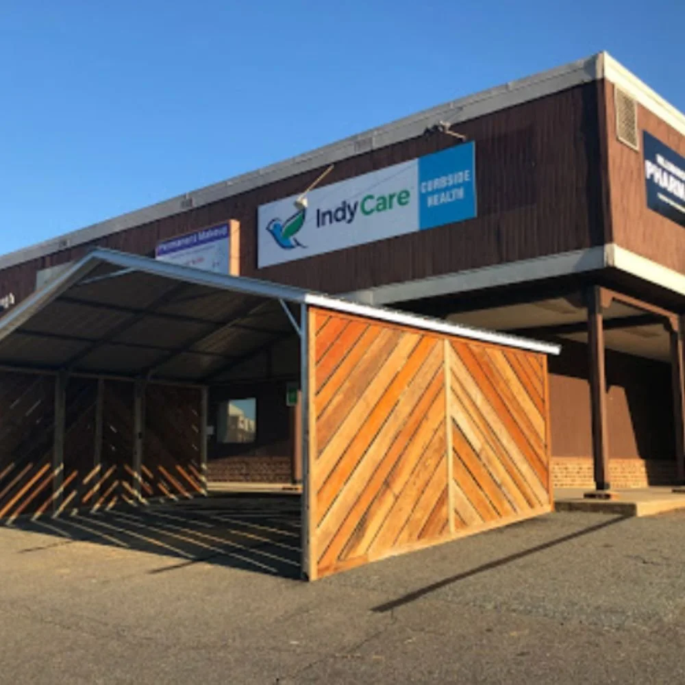 Building with signs for IndyCare and Curbside Health, featuring a wooden shaded entrance and a clear blue sky.