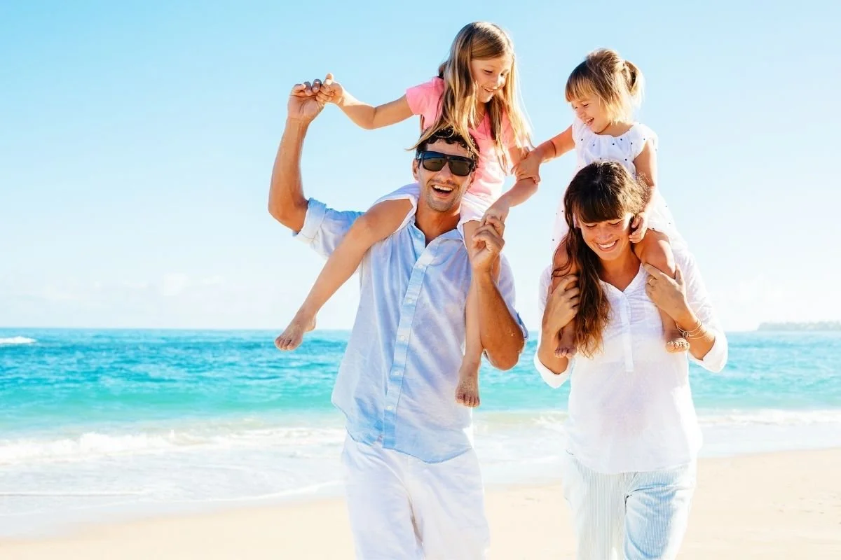 Family with two children on their shoulders, playing on the beach.
