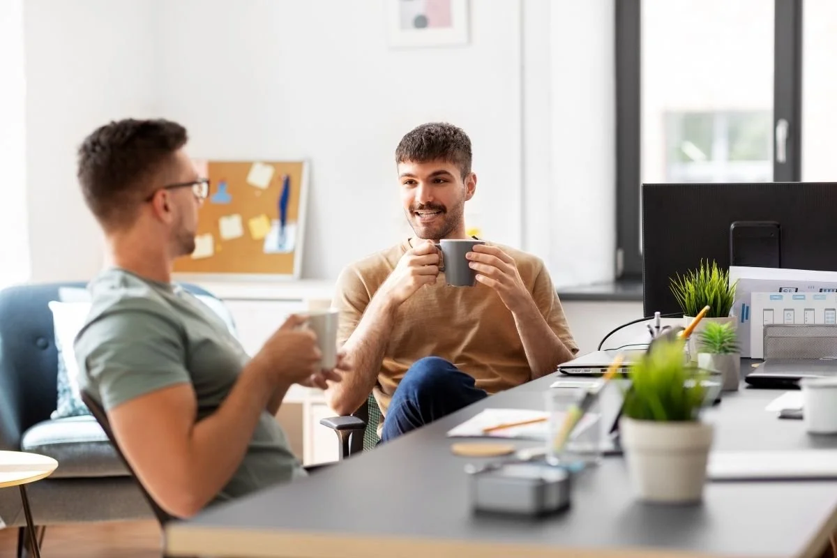 Two male coworkers drinking coffee at a desk.