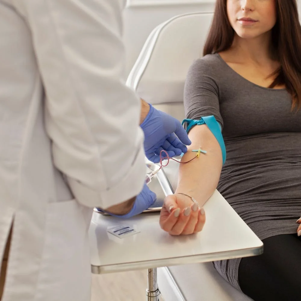 A woman donating blood while seated, with a healthcare worker preparing her arm for the blood draw.