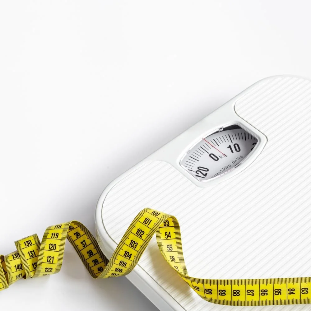 A white bathroom scale with a yellow measuring tape on top of it, showing a measurement of approximately 105 pounds.