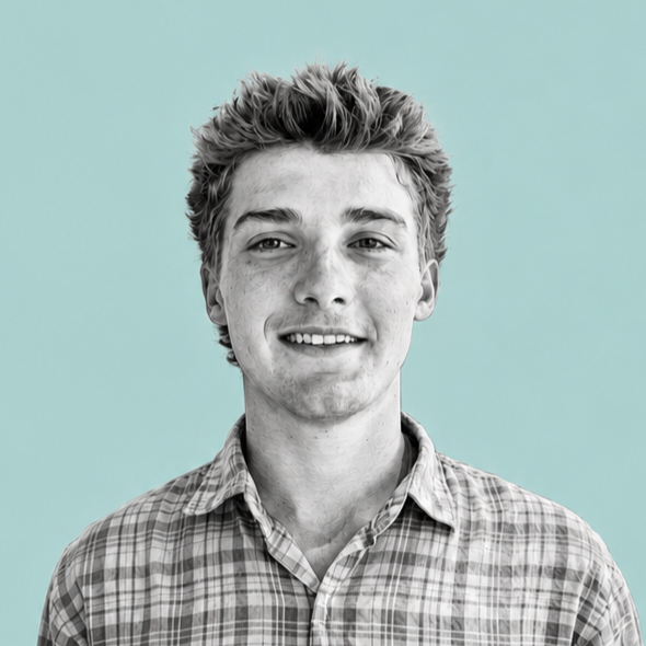 A young man with light skin, curly blonde hair, and freckles, smiling and wearing a checkered shirt against a light blue background.
