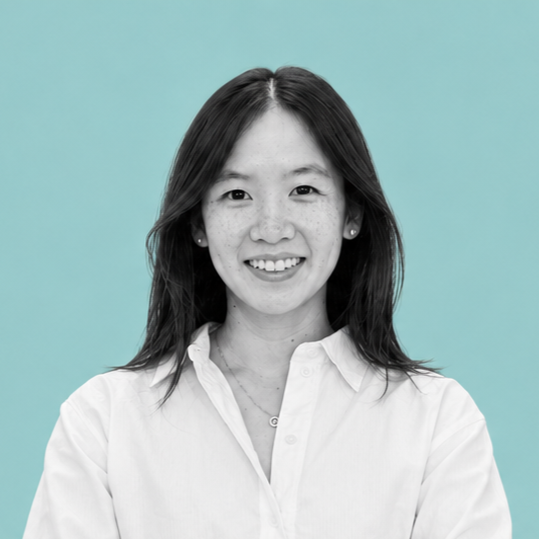 A portrait of a young Asian woman with shoulder-length dark hair, smiling, wearing a white button-up shirt, against a turquoise background.