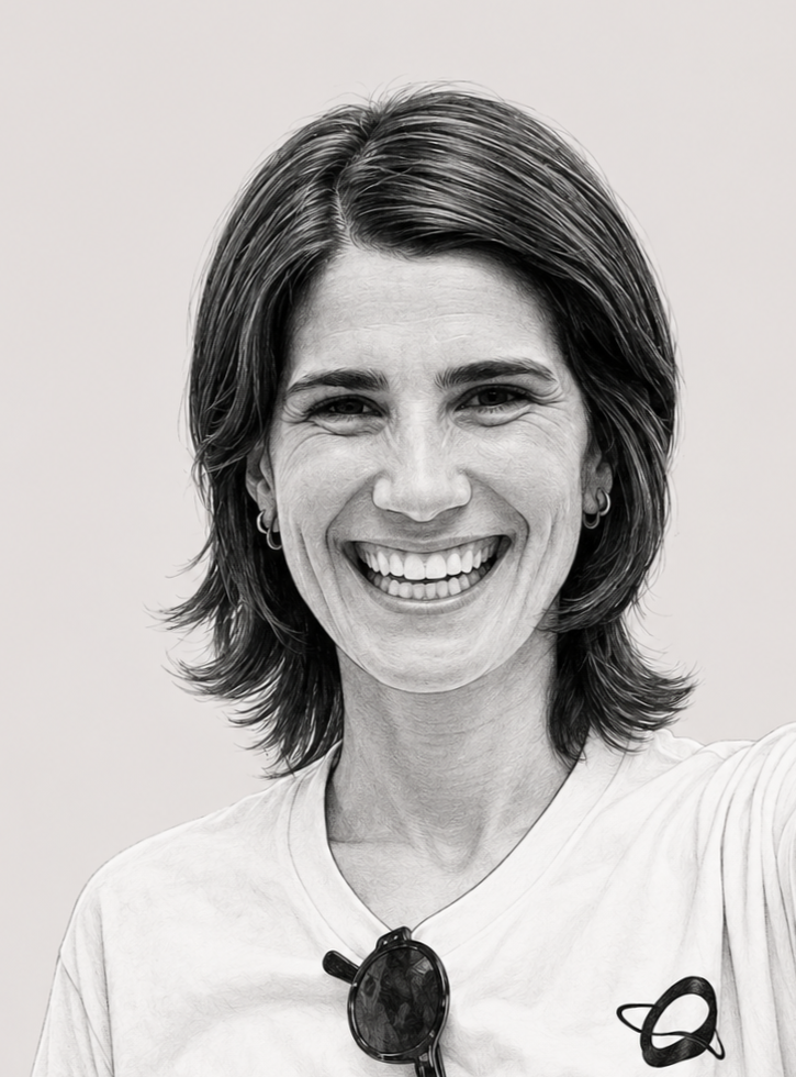 A woman with shoulder-length hair smiling and taking a selfie, wearing a white T-shirt with a small logo and sunglasses hanging from the collar.