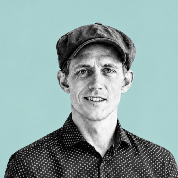 Black and white portrait of a smiling man wearing a polka dot shirt and a flat cap against a light blue background.