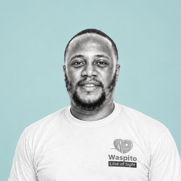 A man with a beard and mustache wearing a white T-shirt with a logo and text, standing against a light blue background.