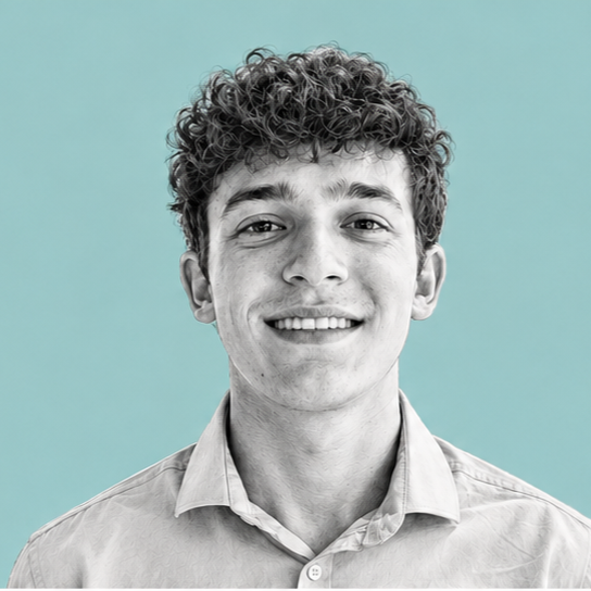 A young man with curly hair smiling in front of a solid light teal background.