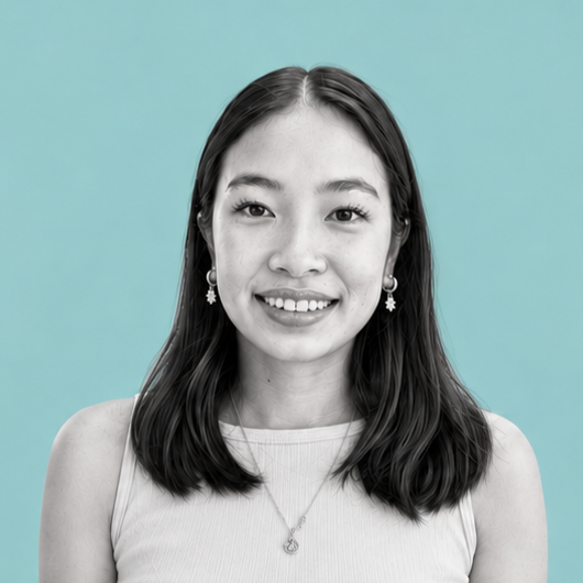 Black and white portrait of a young woman with shoulder-length dark hair, smiling, wearing earrings, a necklace, and a sleeveless top, with a plain blue background.