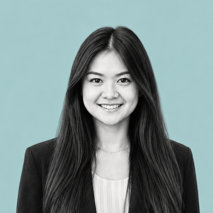 A woman with long dark hair smiling in front of a light teal background, wearing a black blazer and a white top.