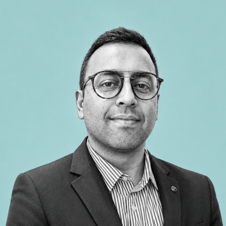 A professional man wearing glasses, a striped shirt, and a blazer, posing against a light blue background.