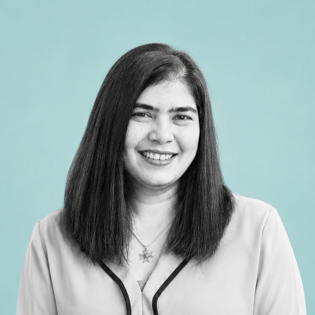 A young woman with long dark hair smiling, wearing a light-colored blazer and a star-shaped necklace, against a light blue background.