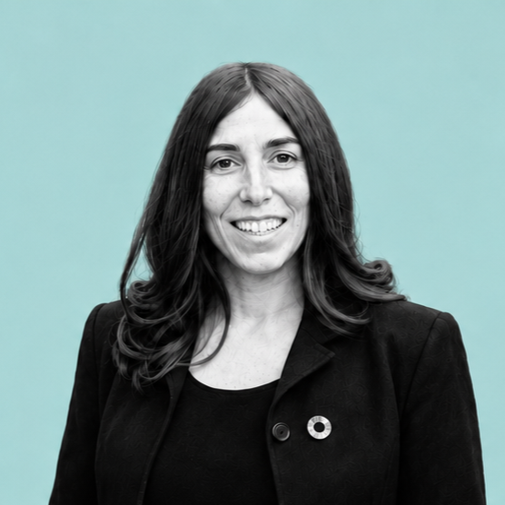 Portrait of a woman with shoulder-length hair wearing a black blazer, smiling against a teal background.