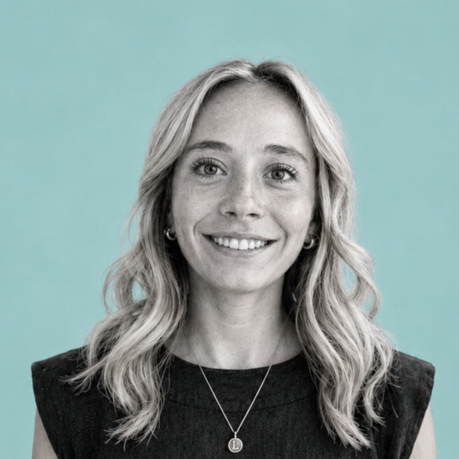 A woman with wavy blonde hair, smiling, wearing a black shirt and a necklace, with a light blue background.