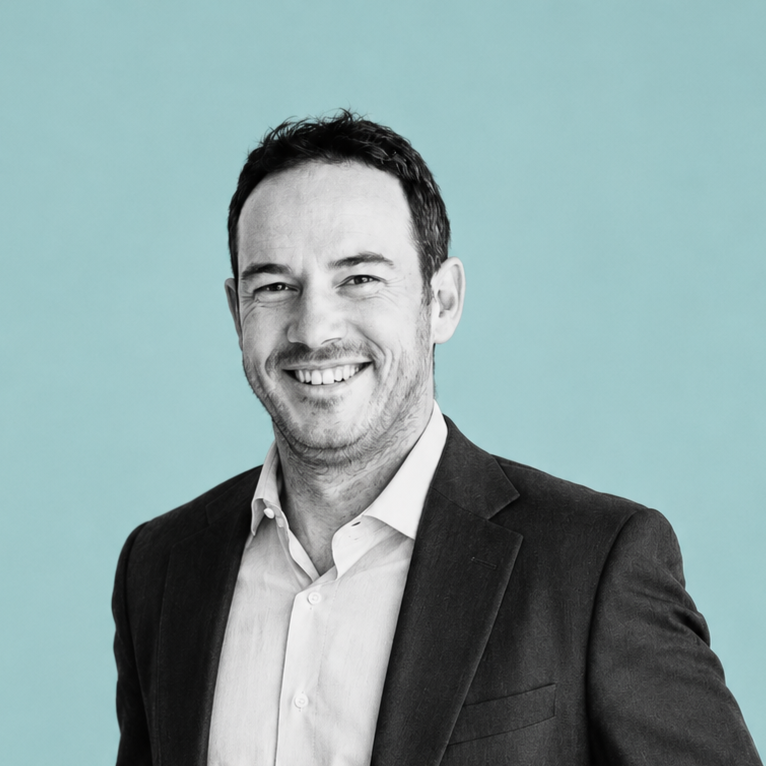 Portrait of a smiling man in a suit jacket and white shirt, against a light blue background.