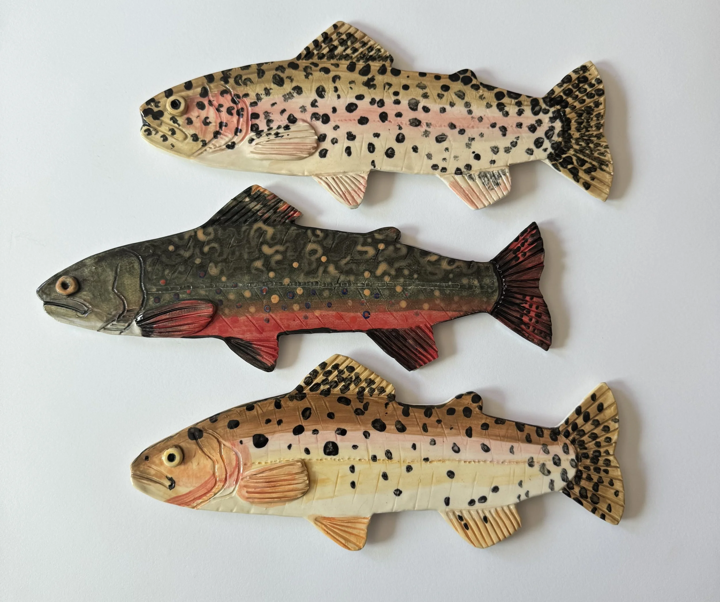 Four carved wooden fish plaques with painted patterns, arranged vertically on a white background.