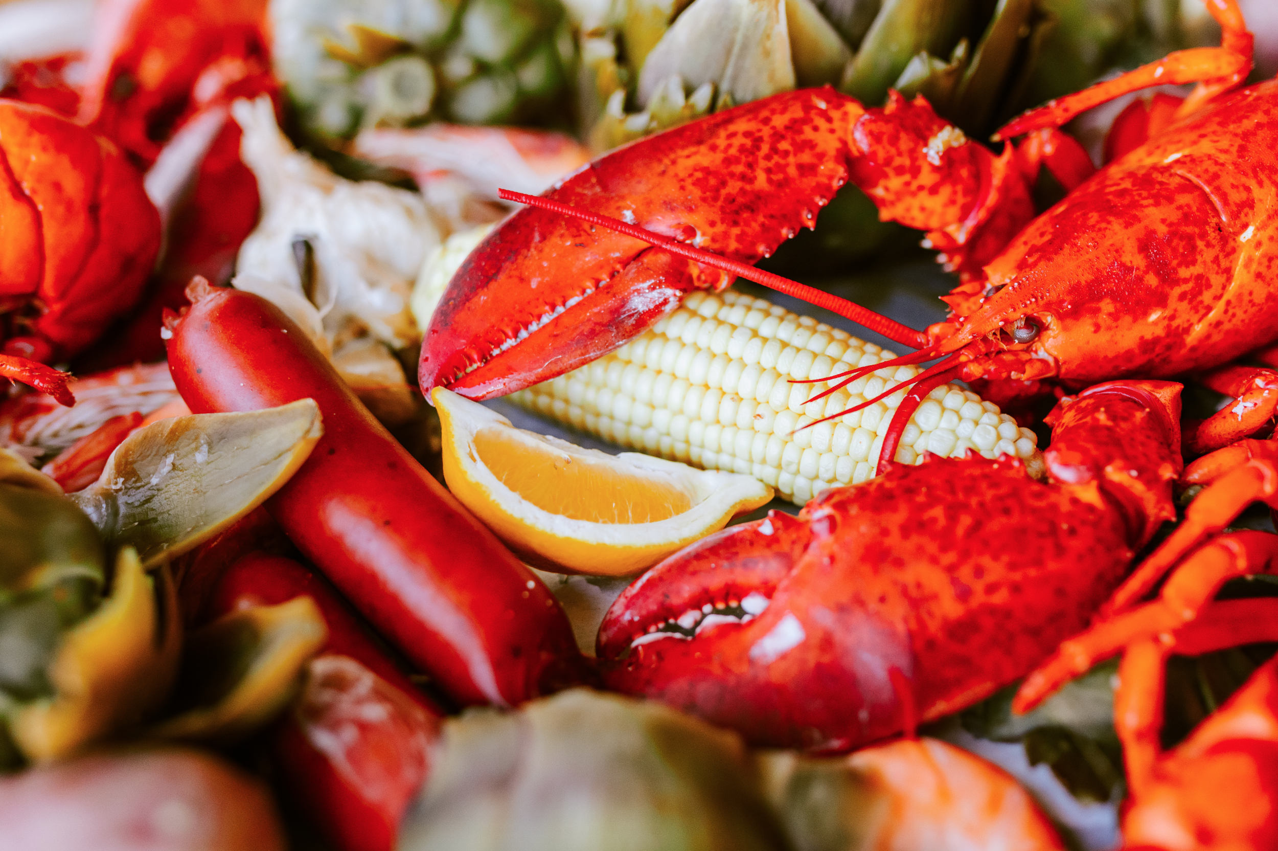 Lobster, corn on the cob, orange wedge, and other seafood items on a platter.