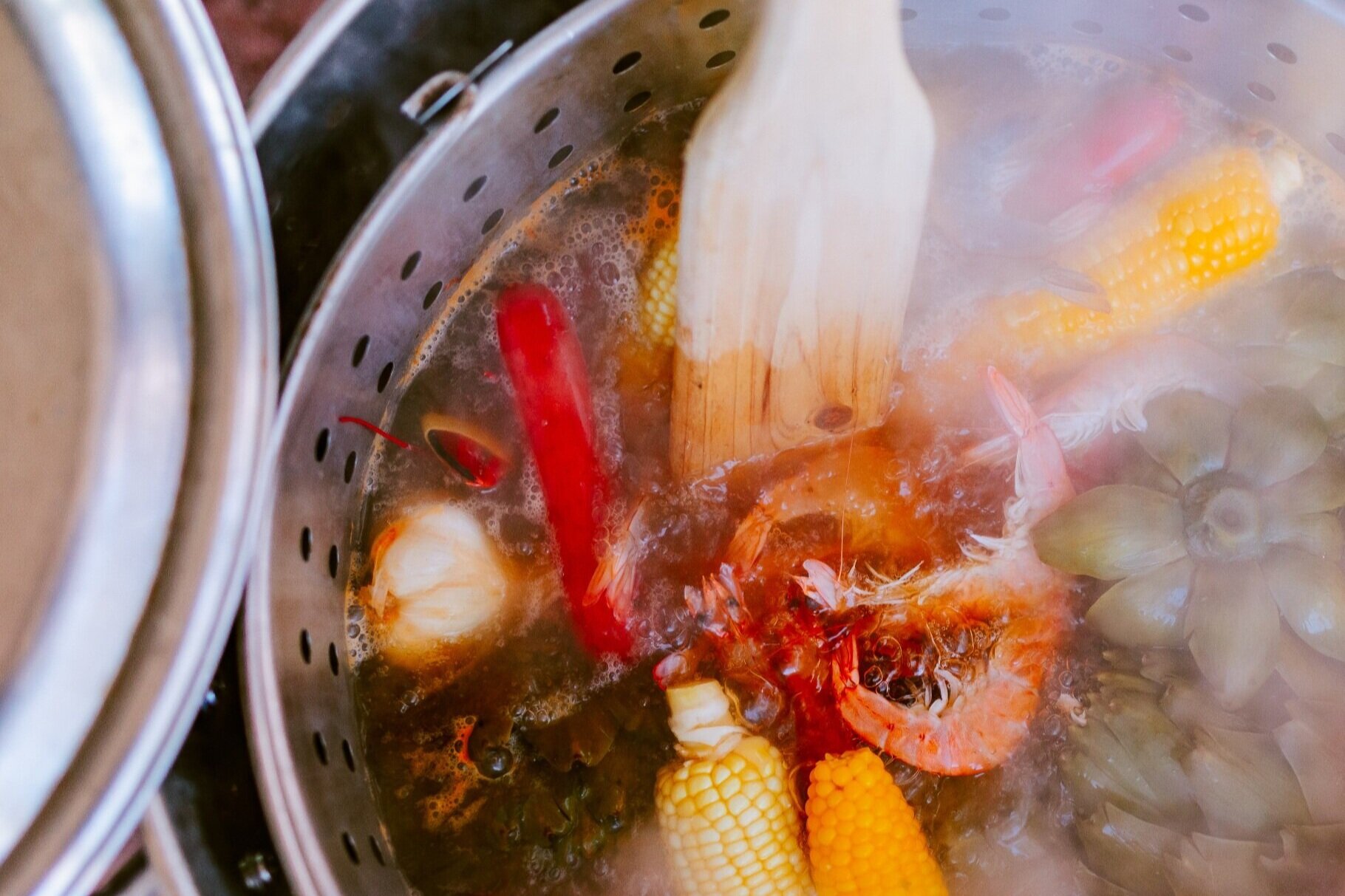 Boiling seafood and vegetables, including corn on the cob, in a metal pot with a steamer insert.