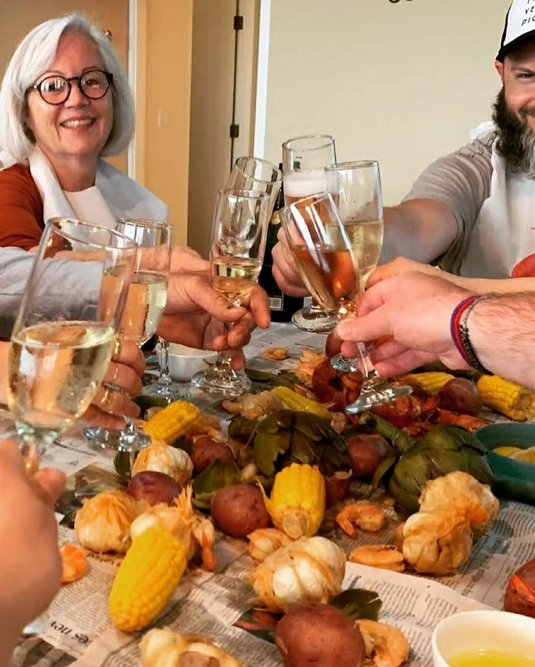 People celebrating with glasses of champagne at a dinner table decorated with corn, artichokes, and other vegetables.