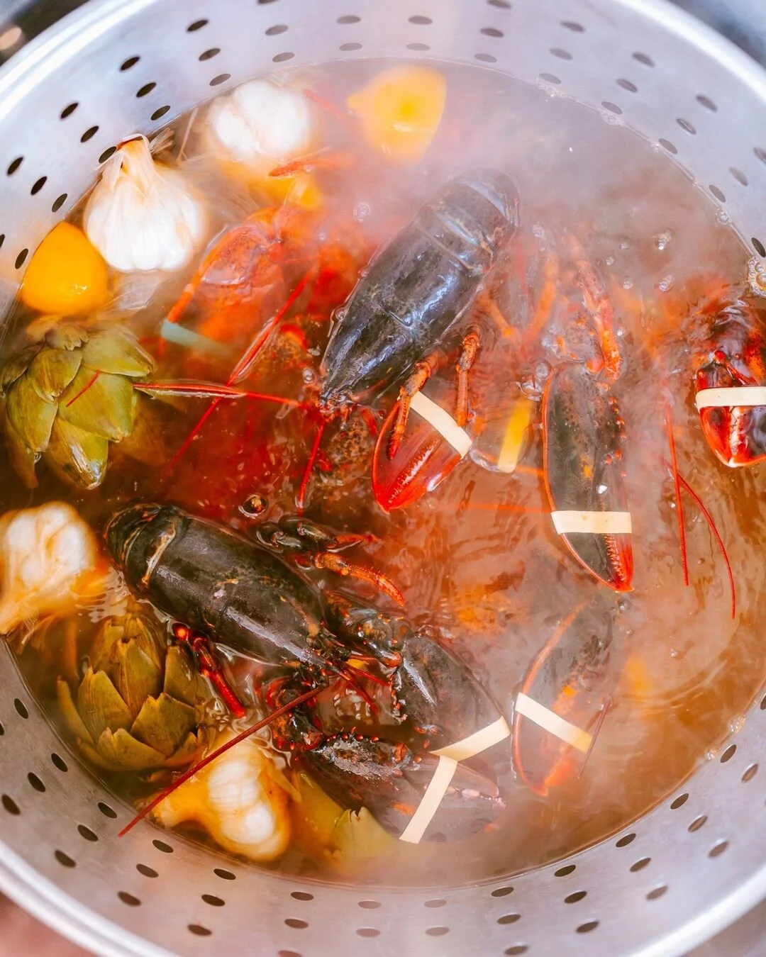 Lobsters, crawfish, clams, and garlic soaking in boiling water, likely for cooking seafood boil.