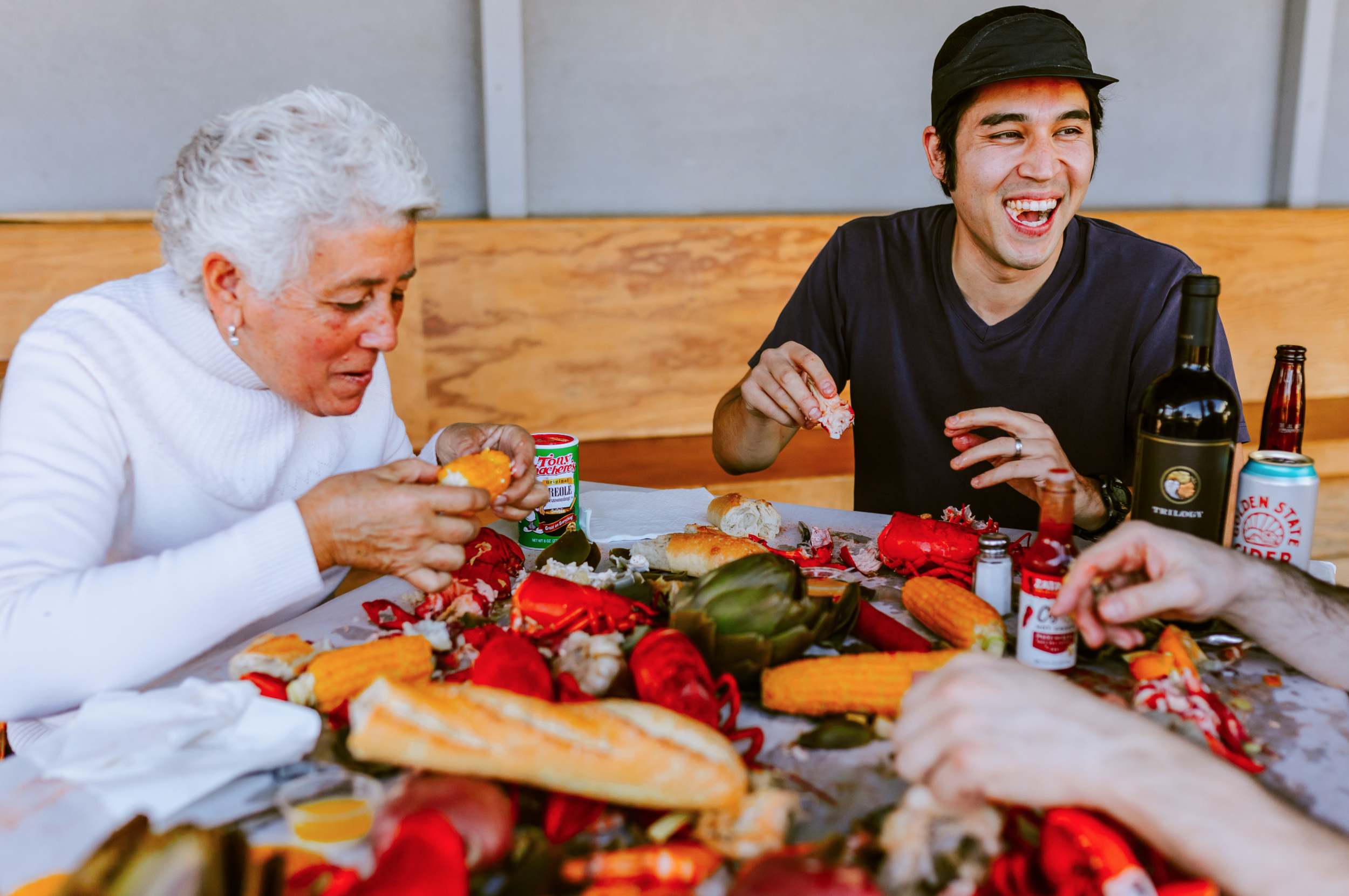 A family dinner with seafood, corn on the cob, bread, and drinks, with two people smiling and enjoying their meal.