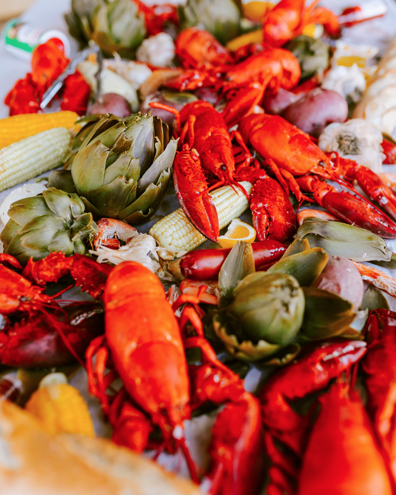 Various cooked seafood, including lobsters, crawfish, and clams, with corn on the cob and lemon wedges.