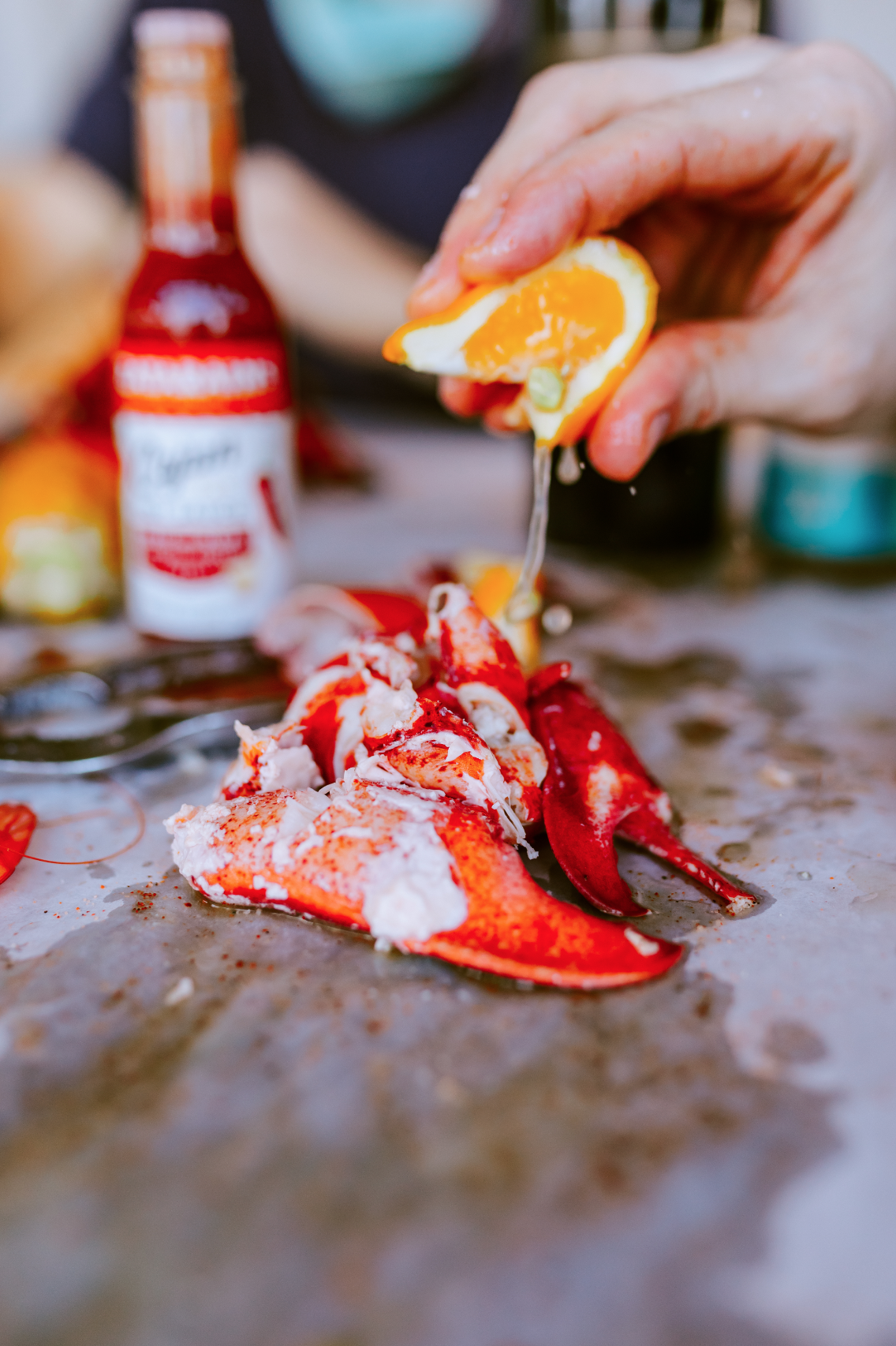 A hand squeezing lemon over lobster claws on a table.