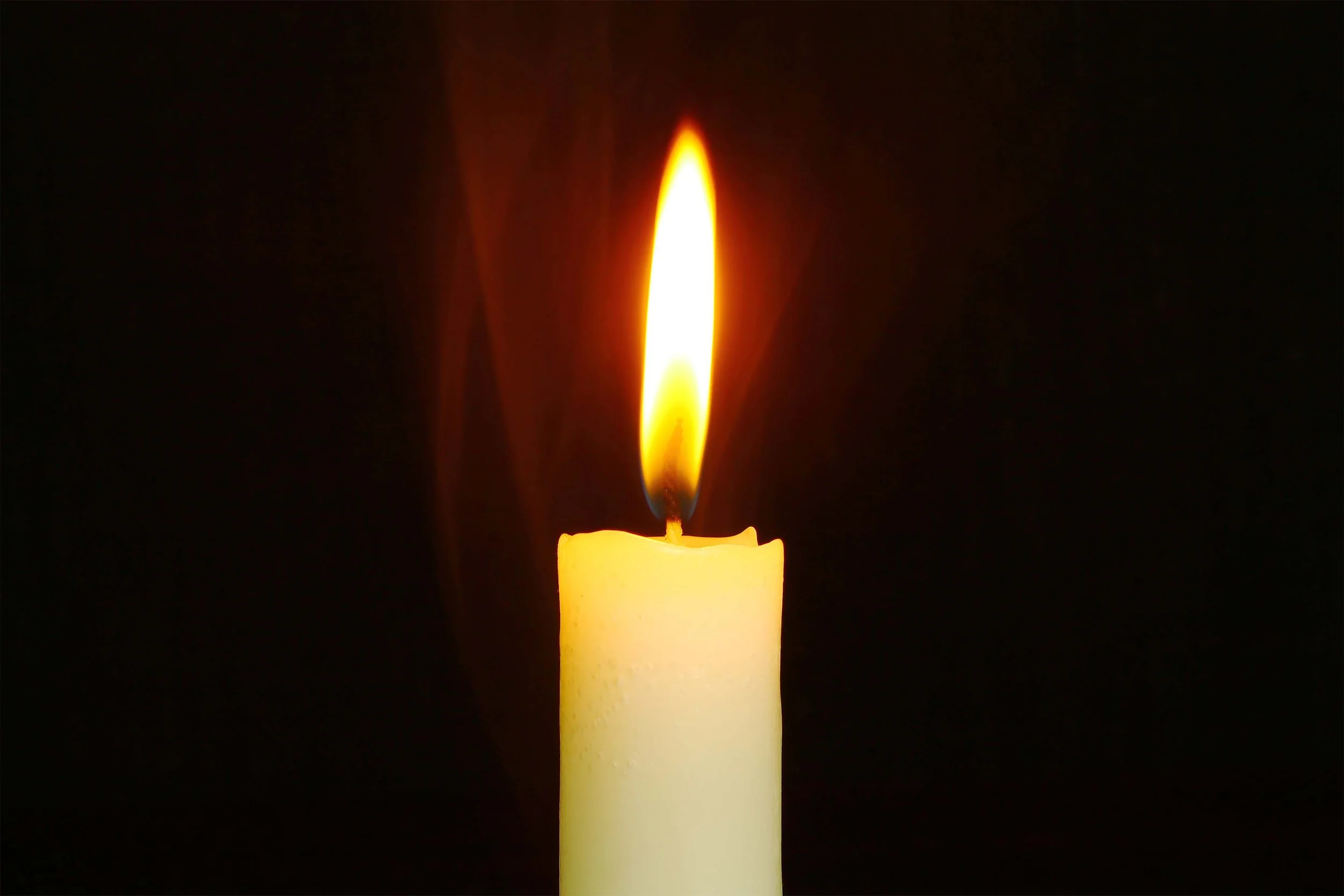 A lit yellow candle with a bright flame against a dark background.