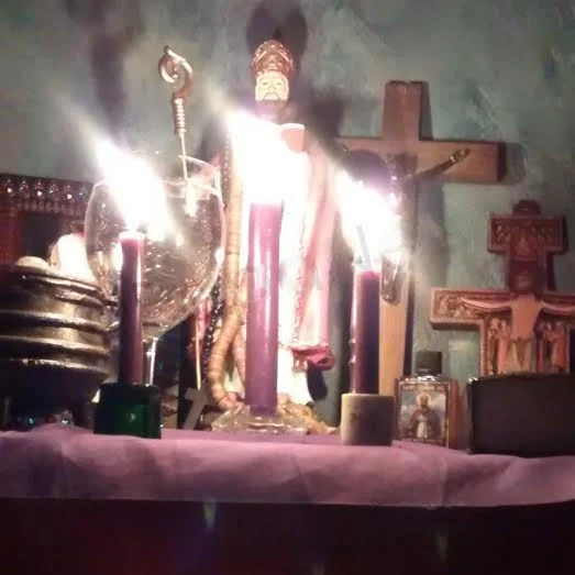 An altar with a religious statue, lit candles, and various religious symbols.