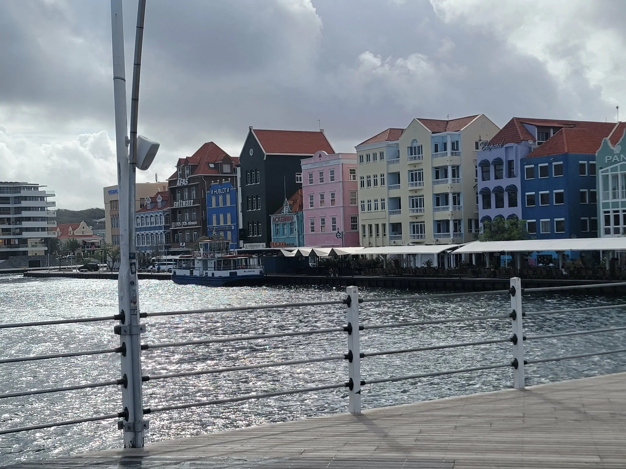 Colorful European-style houses by a river with a boat docked nearby, under a cloudy sky.