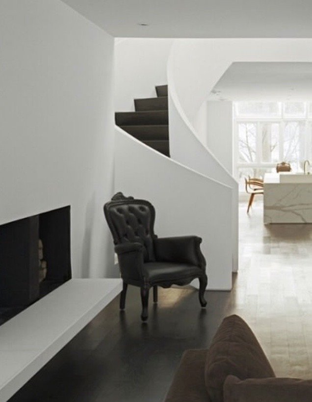 Modern living room with a black armchair, a fireplace, a brown sofa, and a spiral staircase, with a bright window in the background.