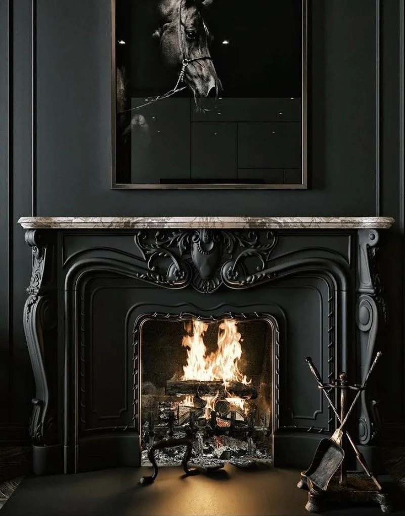 A black ornate fireplace with a fire burning inside, topped with a dark marble mantel. Above it hangs a large black and white photograph of a horse's head. To the right of the fireplace is a set of fireplace tools, including a poker and tongs.