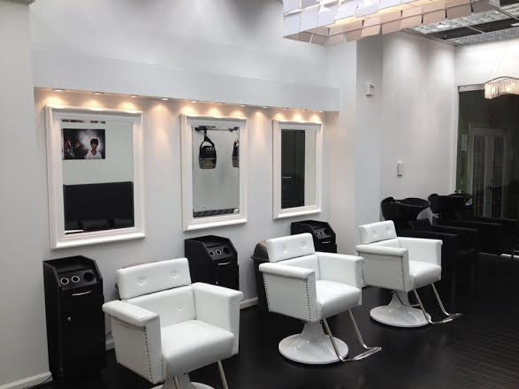 Modern hair salon with three white styling chairs, black washbasins, and mirrors with lighting in a clean, minimalist space.