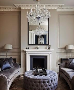 Elegant living room with chandelier, mirror, white fireplace, and plush velvet couches