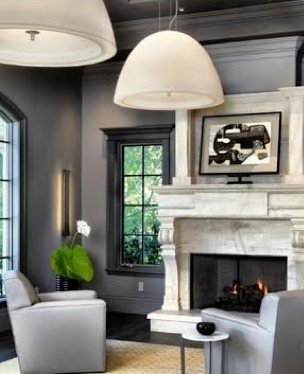 Living room with gray walls, a white fireplace, black-framed windows, a white armchair, and a white side table with a black bowl.