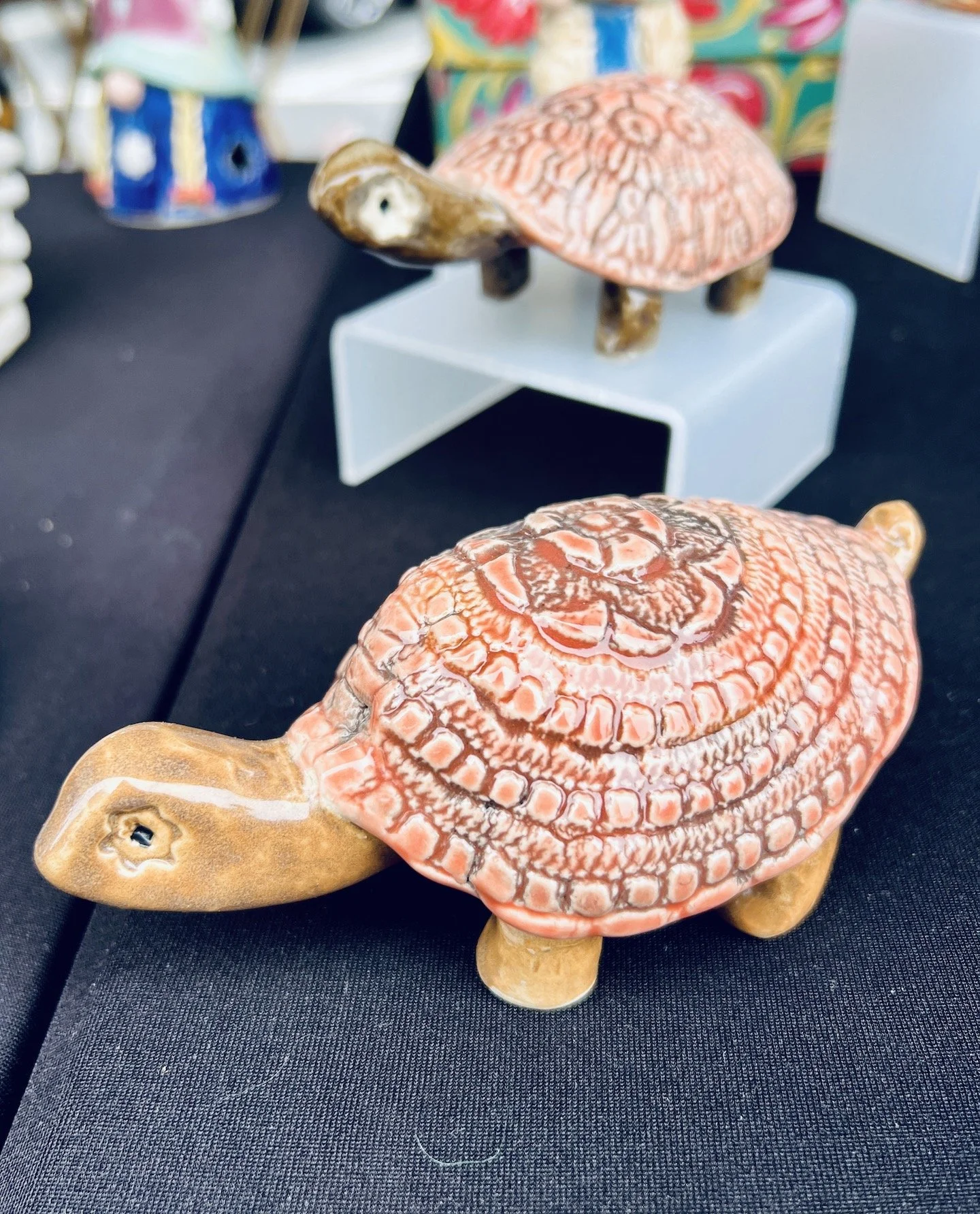 Wooden turtle sculpture with a pink, scaled shell and light brown limbs, placed on a black surface.