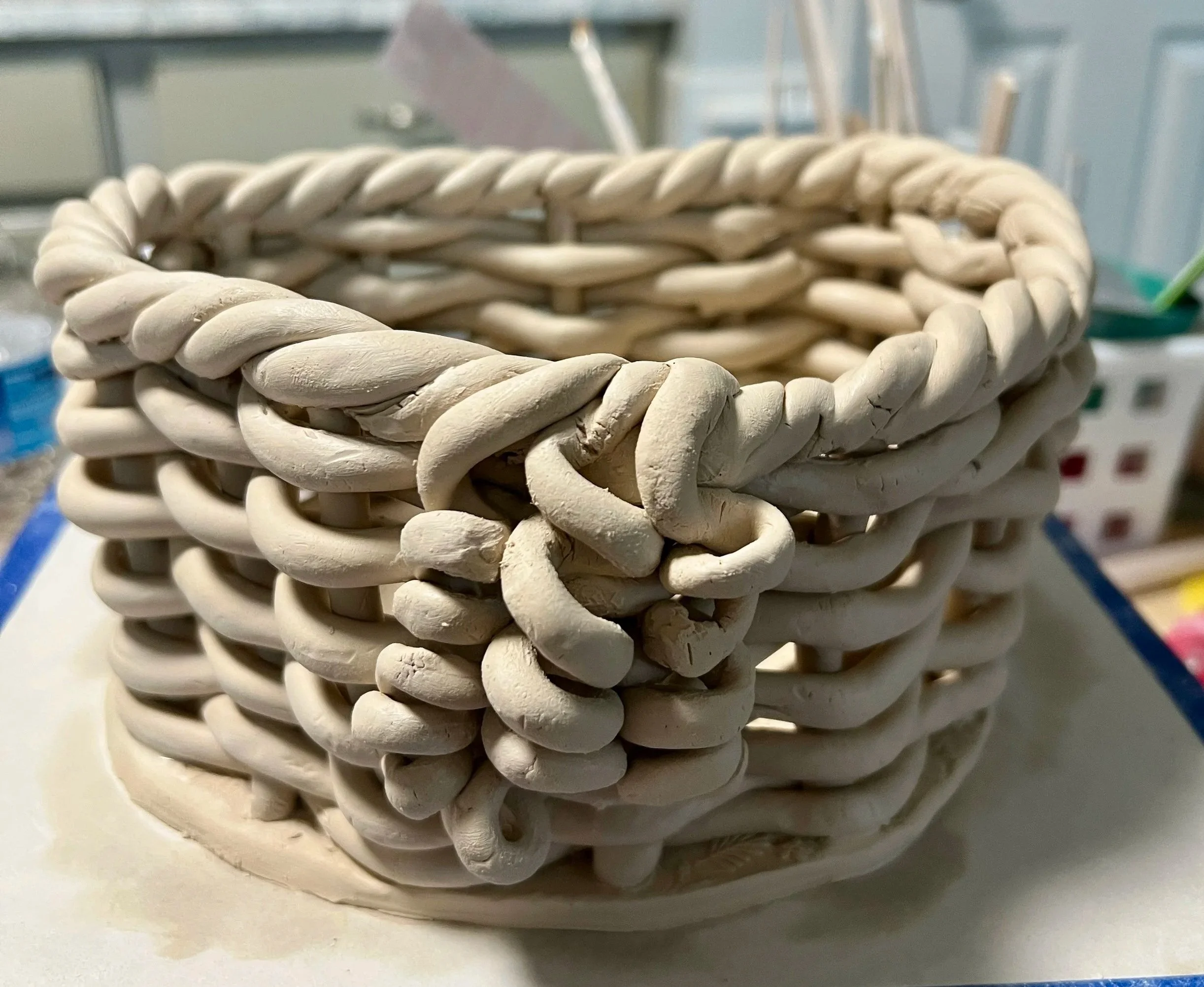 Close-up of intricately braided white ceramic or clay basket with a tight, woven pattern, placed on a light-colored clay.