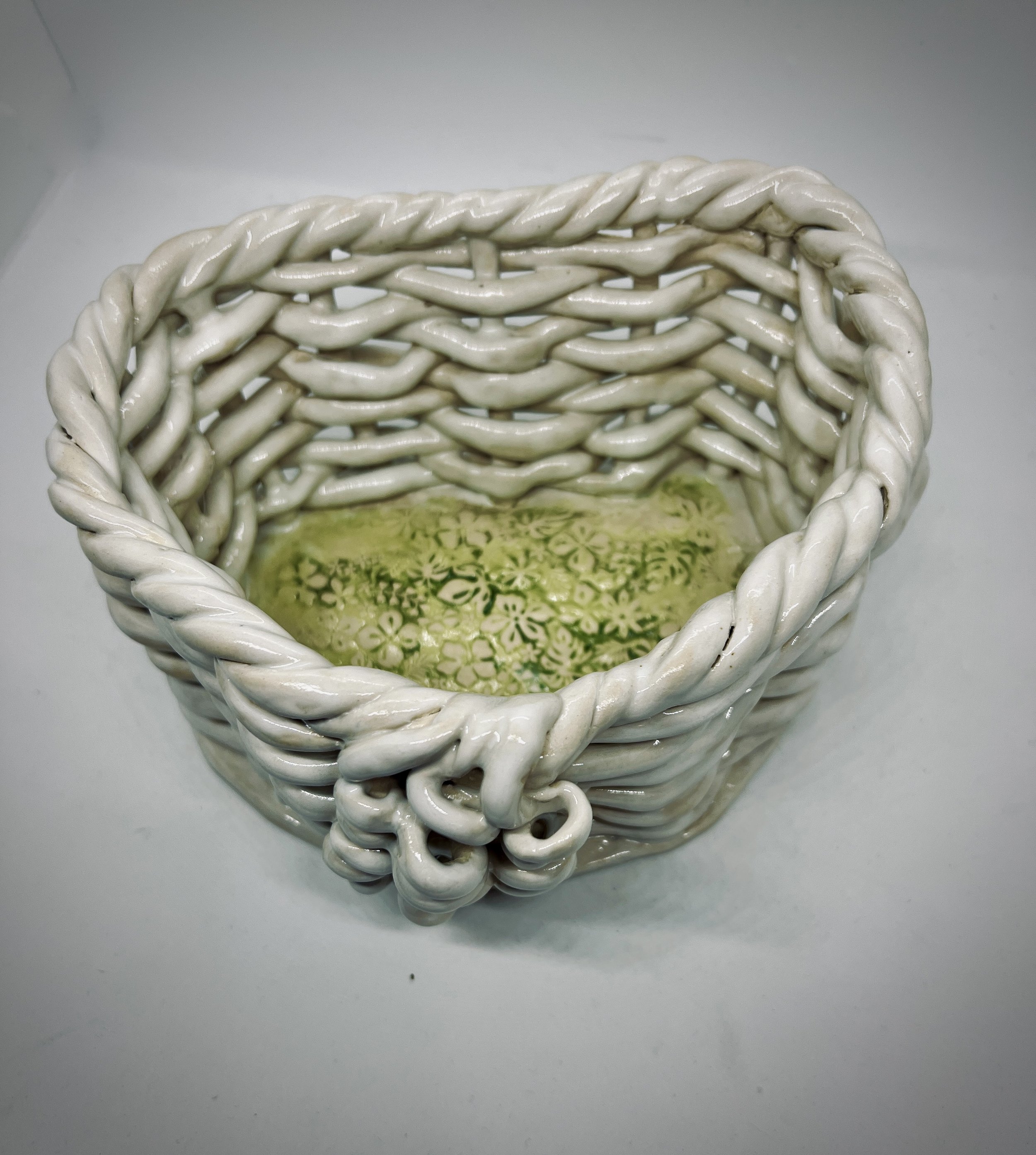 White ceramic basket with twisted handle, sitting on a white surface, with a floral design inside.