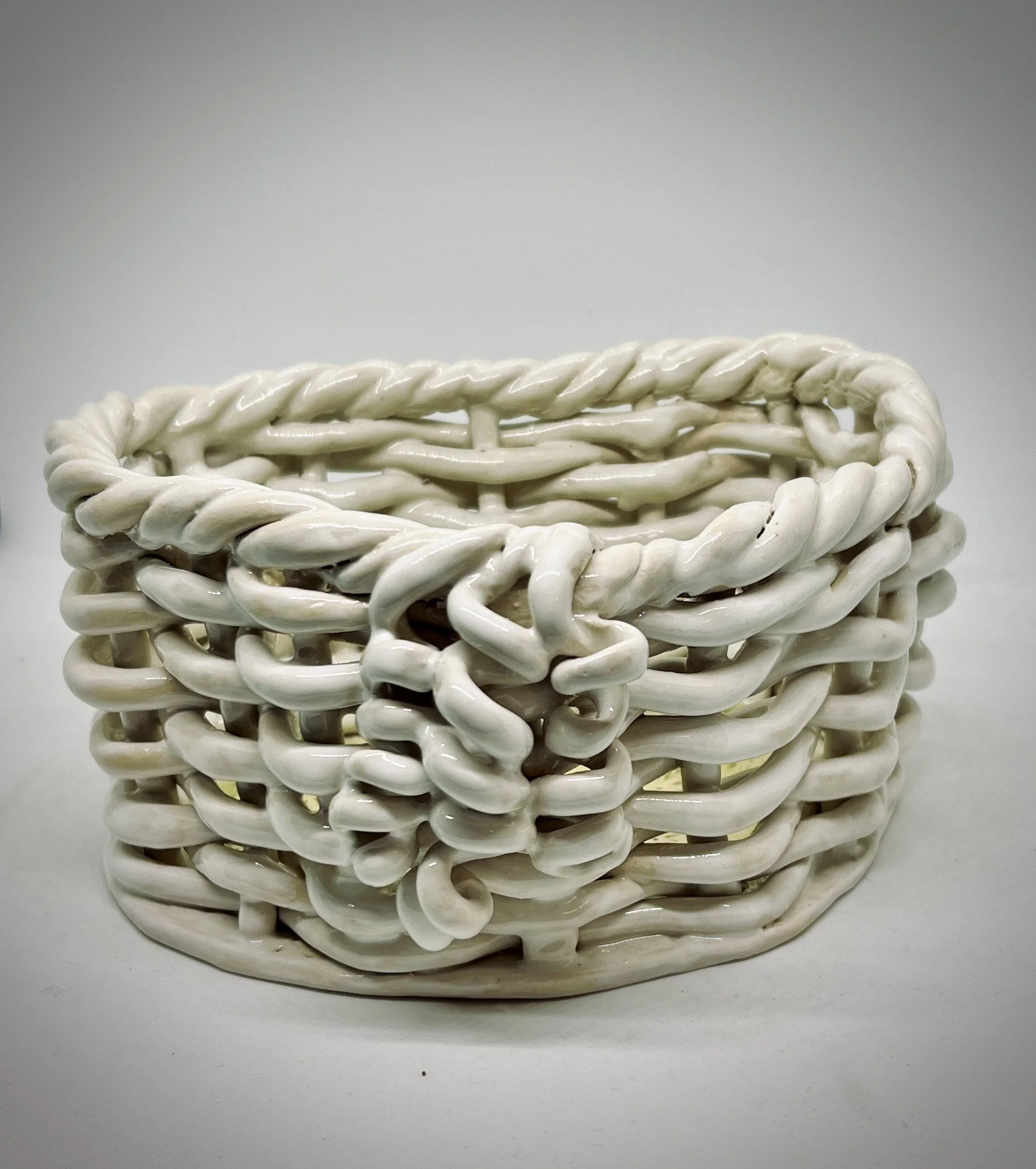 Close-up of a white, woven ceramic basket on a plain white background.