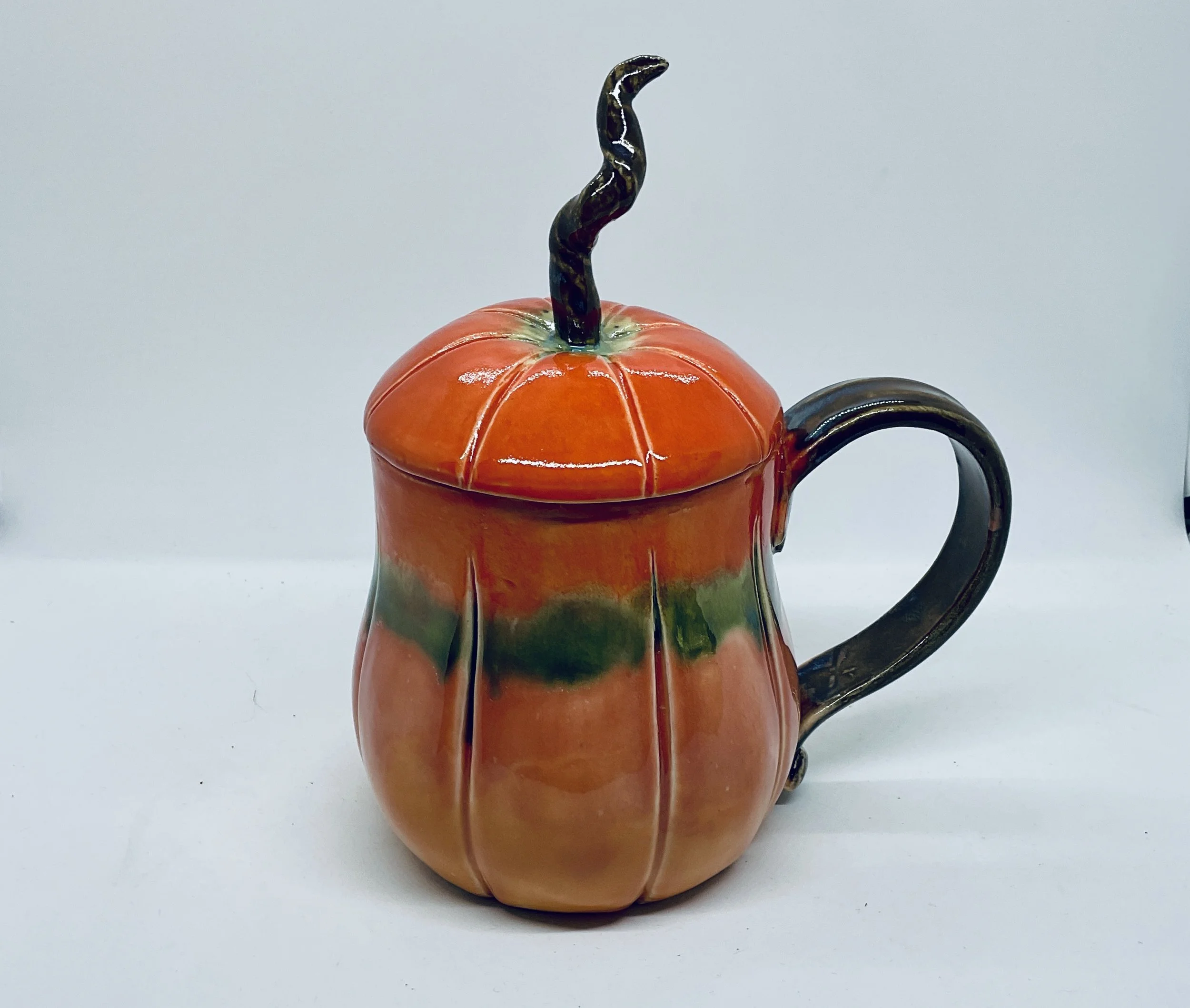 A ceramic teapot shaped like a pumpkin with a twisted black and white handle and a wavy black and white spout, set against a plain background.