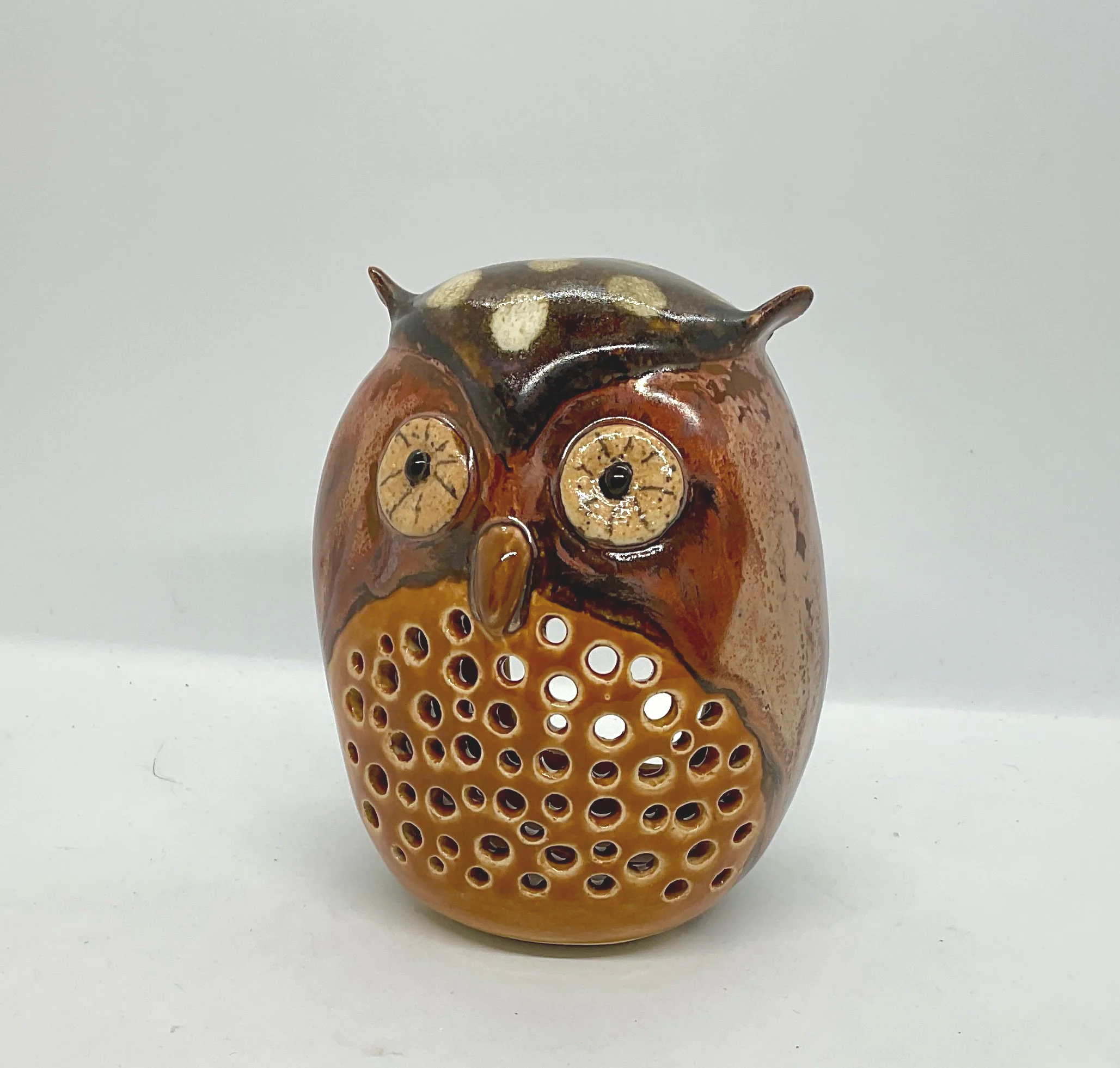 Ceramic owl luminary with detailed carved eyes, beak, wholes in the front to let the light trough with feather patterns on the back sitting against a plain white background.