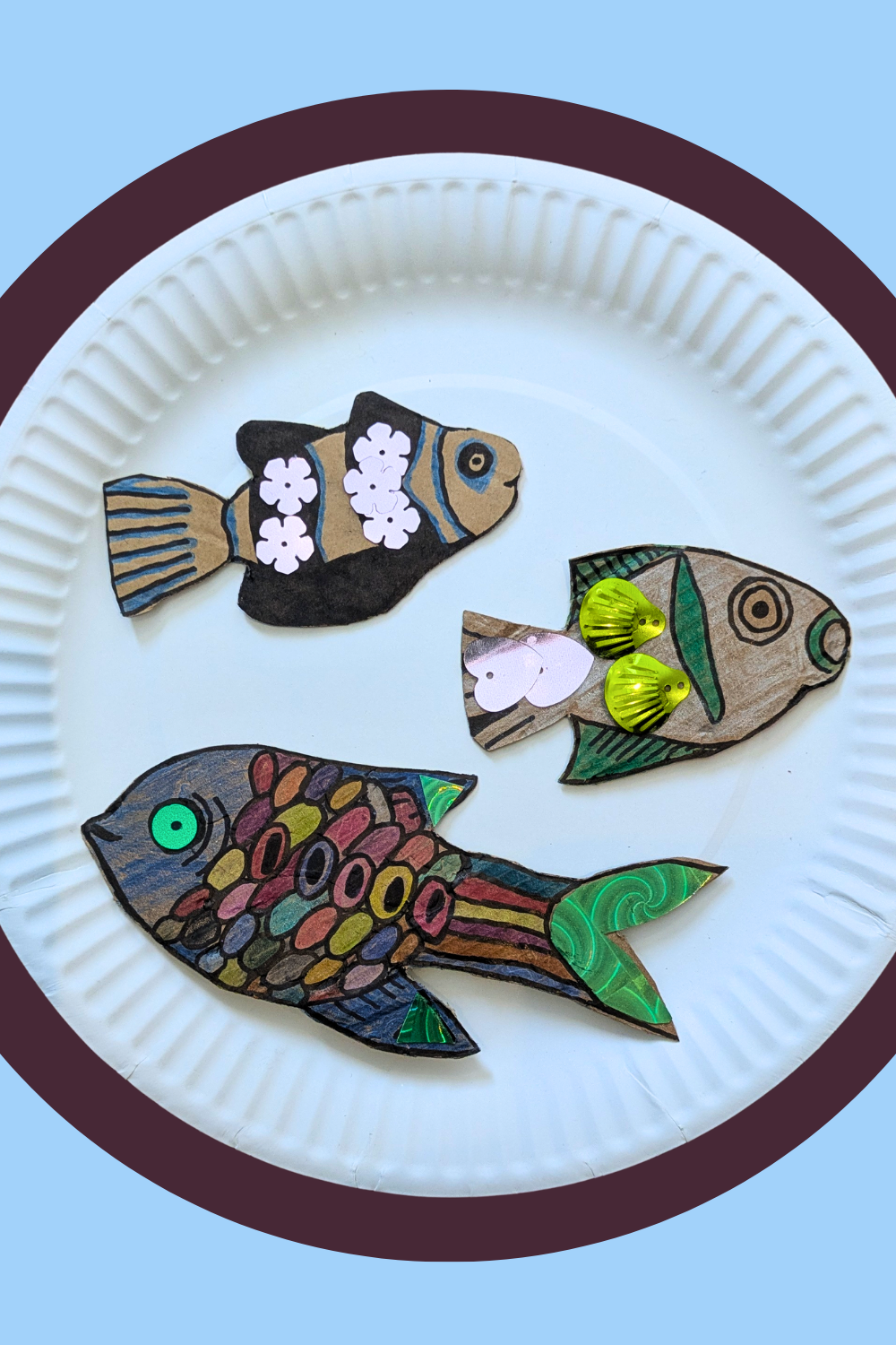  Four handmade cardboard fish with different colourful patterns displayed on a white plate. 